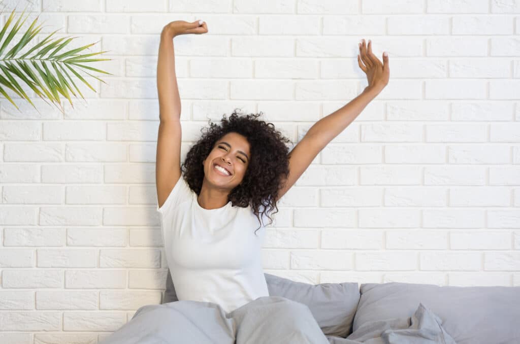 Beautiful african-american woman waking up in her bed, smiling and stretching