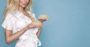 A woman in a white robe holding breast implants