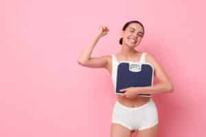 A woman smiling while holding a scale after reaching her weight loss goals