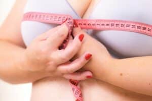 A close-up shot of a woman wrapping a tape measure around her breasts before breast reduction surgery