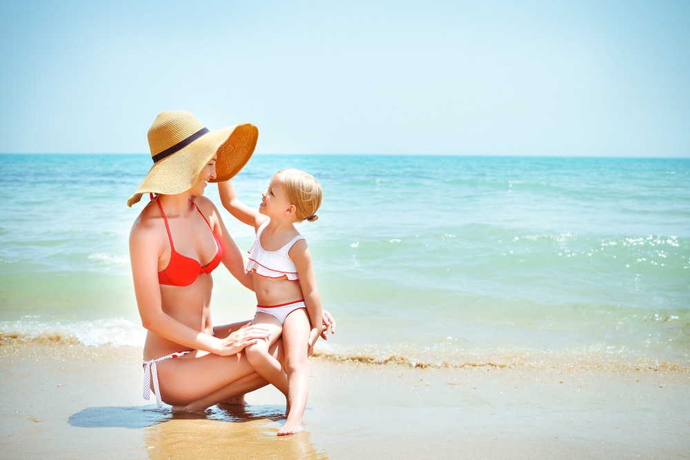 A woman in a bikini playing with her baby after a mommy makeover in Edmond